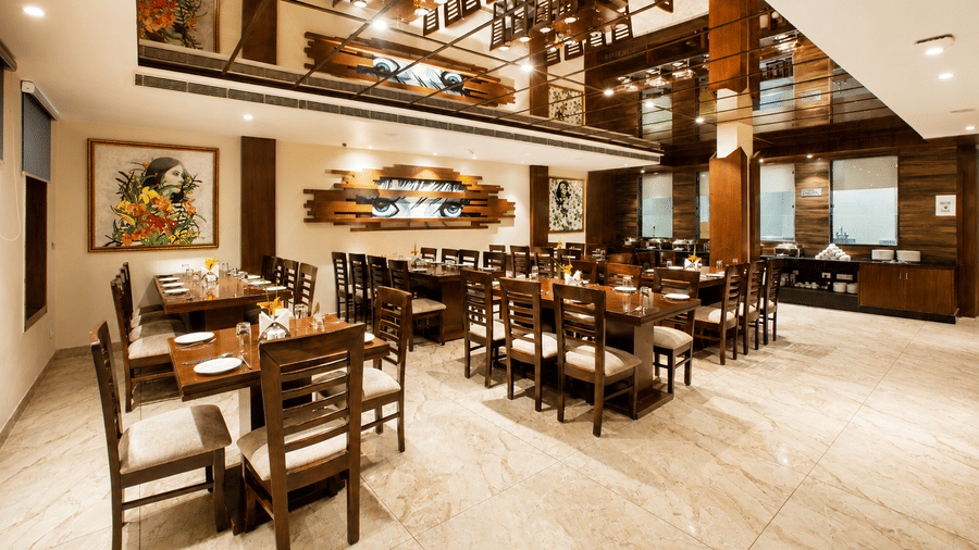 Restaurant dining area with wooden tables, chairs and framed wall art at Eastlynn Resort, Rishikesh.