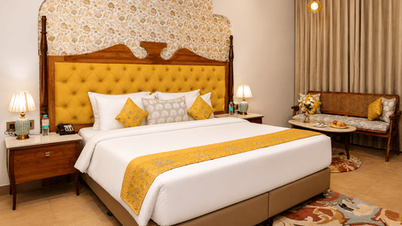 Guest room with a golden tufted headboard, double bed, white bedding, and yellow cushions at Kadamb Kuteer, Vrindavan.