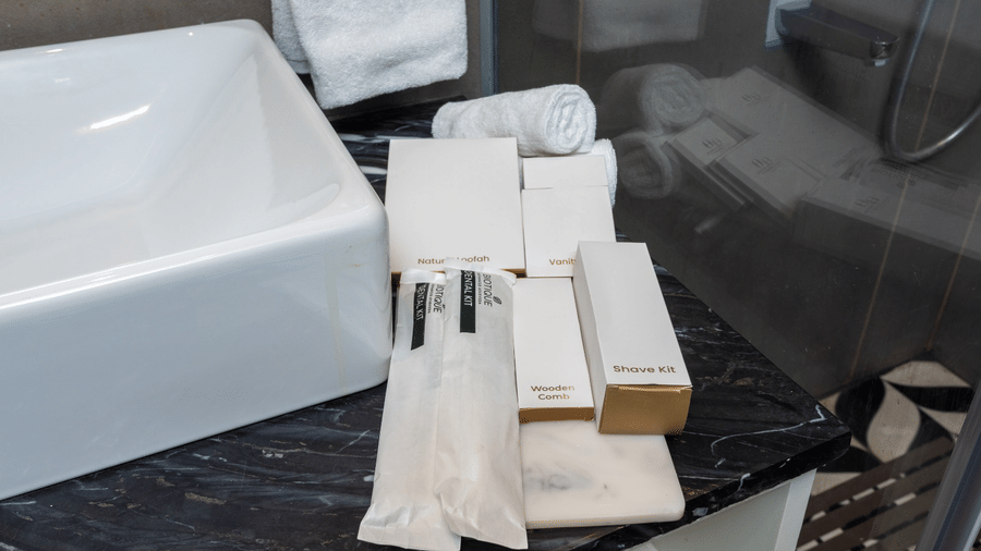 A close-up of a bathroom sink on a black marble counter with packaged toiletries and a towel | Lawrence Solitaire Resort, Nainital