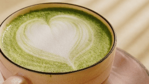 vibrant green matcha latte in a clear glass, featuring white latte art, sitting on a pink saucer at Gemini Continental