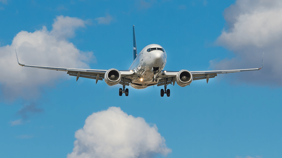 A commercial passenger aeroplane descending through a bright blue sky with white, fluffy clouds.
