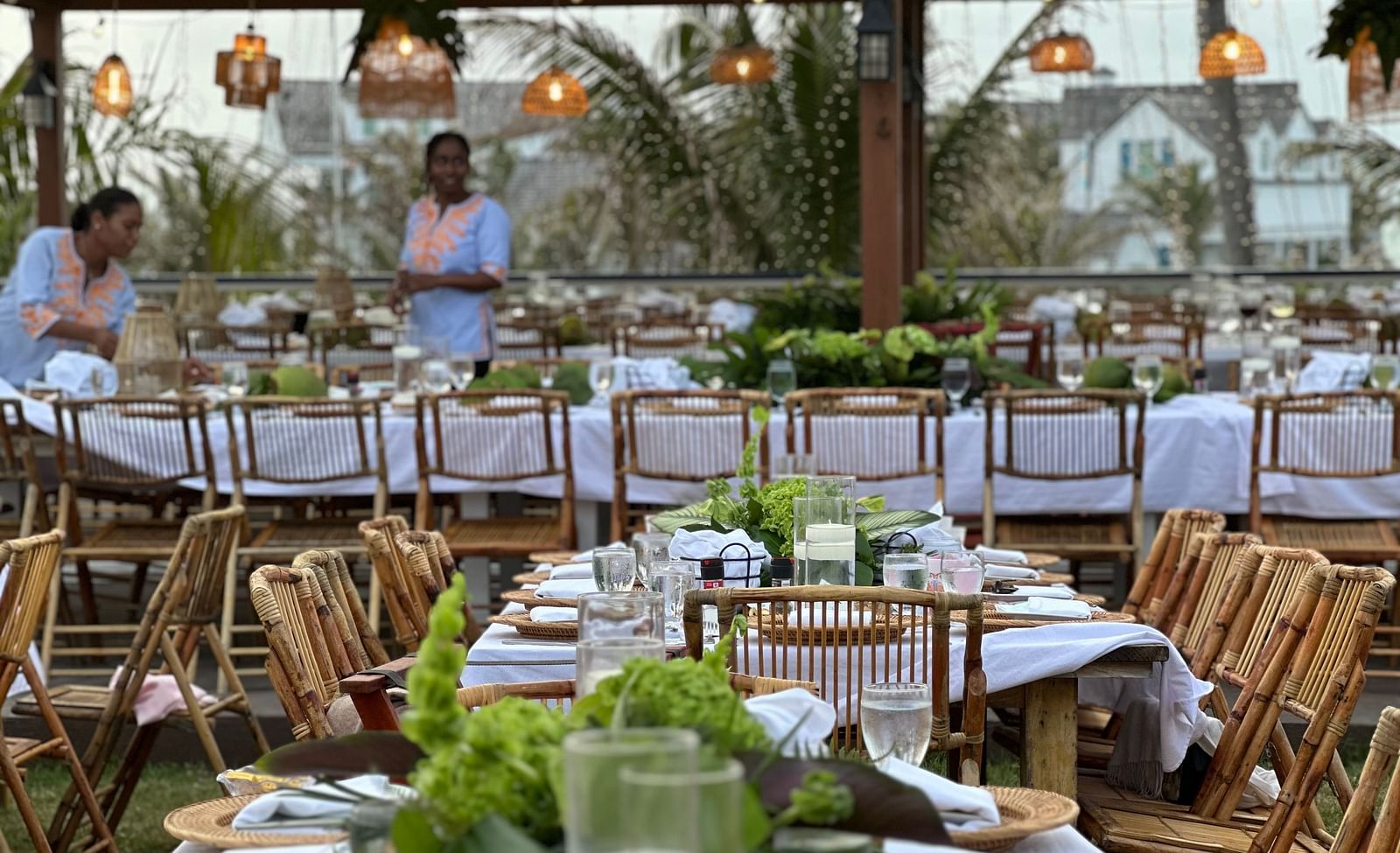 An open dining area featuring several huge dining table paired with wooden chairs. The area is organized for big events like weddings as the tables have bouquets and other decorative elements along with plates and cutlery.