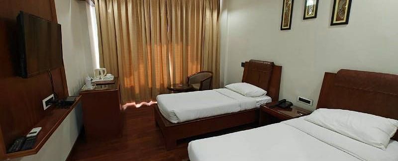 A spacious Luxury Room with two single beds along with beige coloured curtains covering the windows - Hotel Gold, Panipat