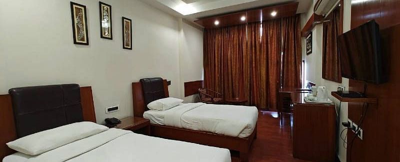 A bedroom with two single beds and dark wooden flooring along with a wall mounted television - Hotel Gold, Panipat
