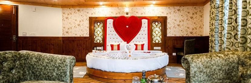 A cosy and inviting hotel room with a circular bed, comfortable sofas, and a romantic heart-shaped decoration | DLS La Serene Manali