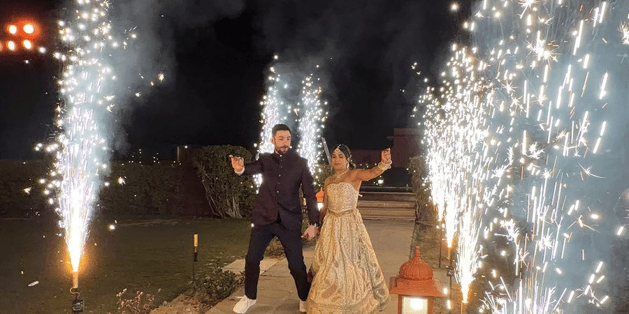 A couple walks down an outdoor pathway at night at Umaid Palace, framed by bright, erupting cold firework sparklers on both sides.