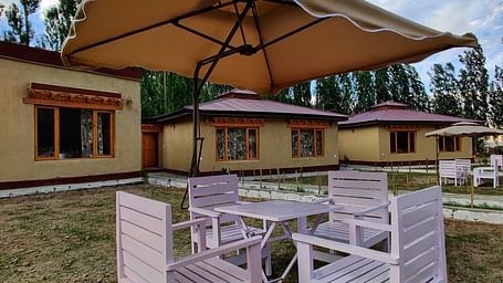 Outdoor seating and tables with umbrellas at the White Sands Resort, Ladakh providing a shaded space with a view of the surrounding landscape.
