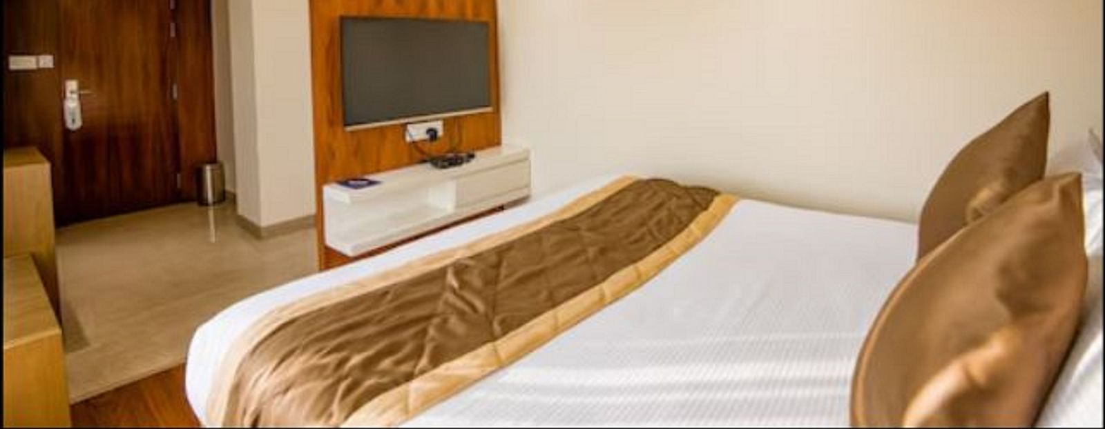 A neatly arranged standard hotel room with a large bed, a wooden headboard, a wall-mounted television, and a colourful painting above the bed at Yashshree The Imperial Inn, Siliguri.