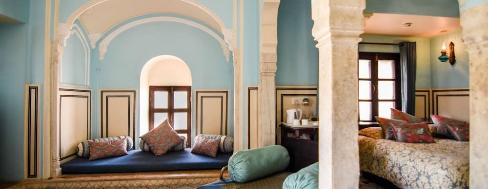 An interconnected suite  at Royal Heritage Haveli with a seating area featuring blue upholstery and a view into a bedroom through an archway.