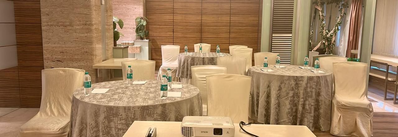 Conference-style setup with covered chairs and a central projector on a table at Mirage Hotel, Mumbai.