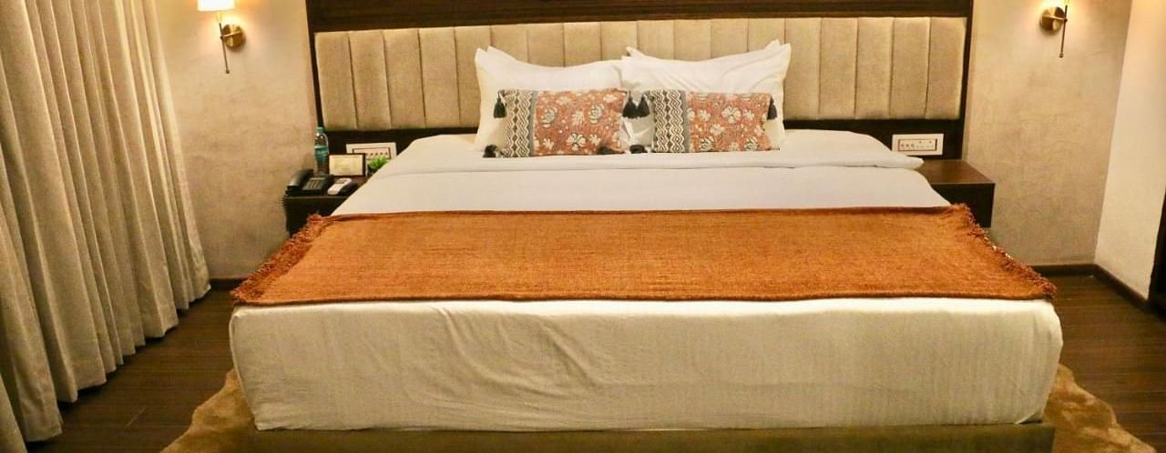 A neatly made bed with white and orange linens of Luxury Junior Suite at Nalapad Hotel Bangalore International.