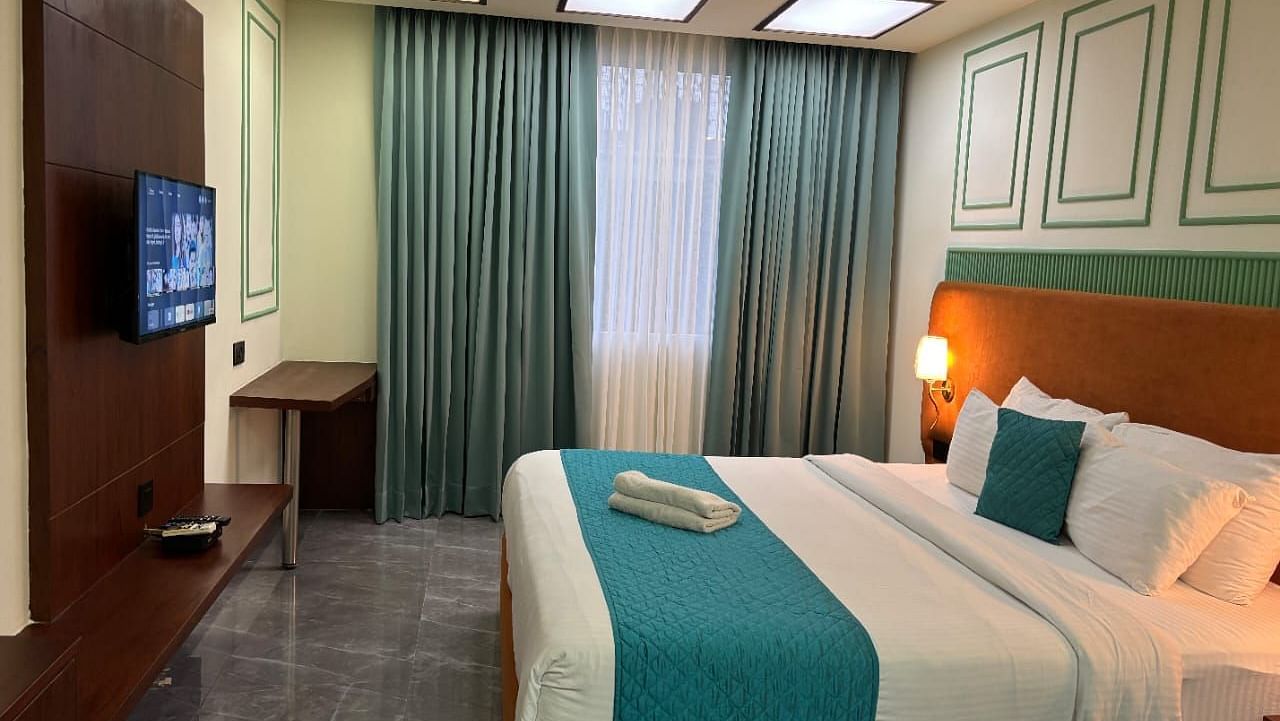 A comfortable room showing a double bed with blue accents, a television, and curtains - Asian Suites IFFCO Metro, Gurgaon