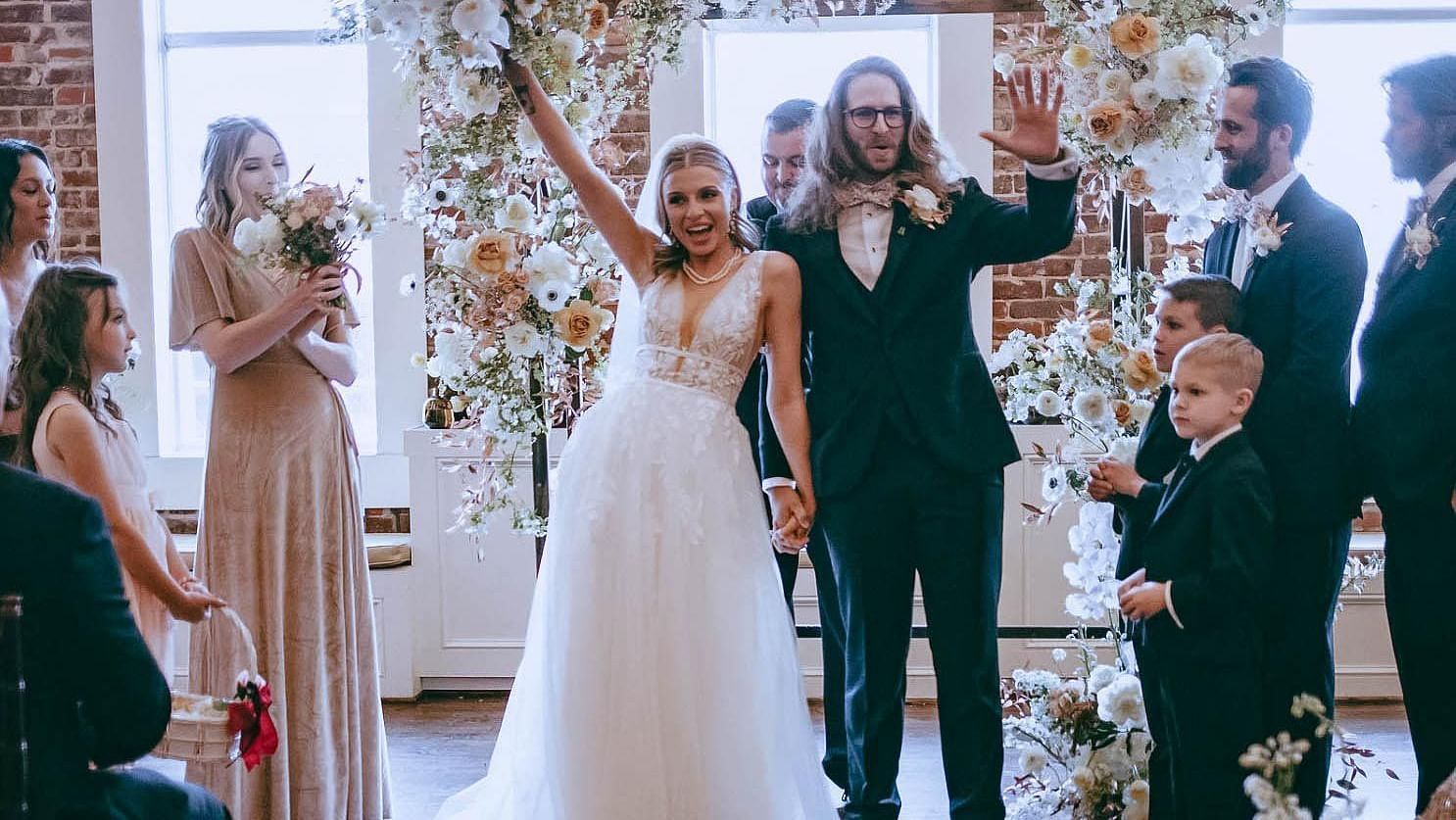  A joyful wedding ceremony with the bride and groom standing in front of their guests, exchanging vows amidst beautiful floral arrangements.