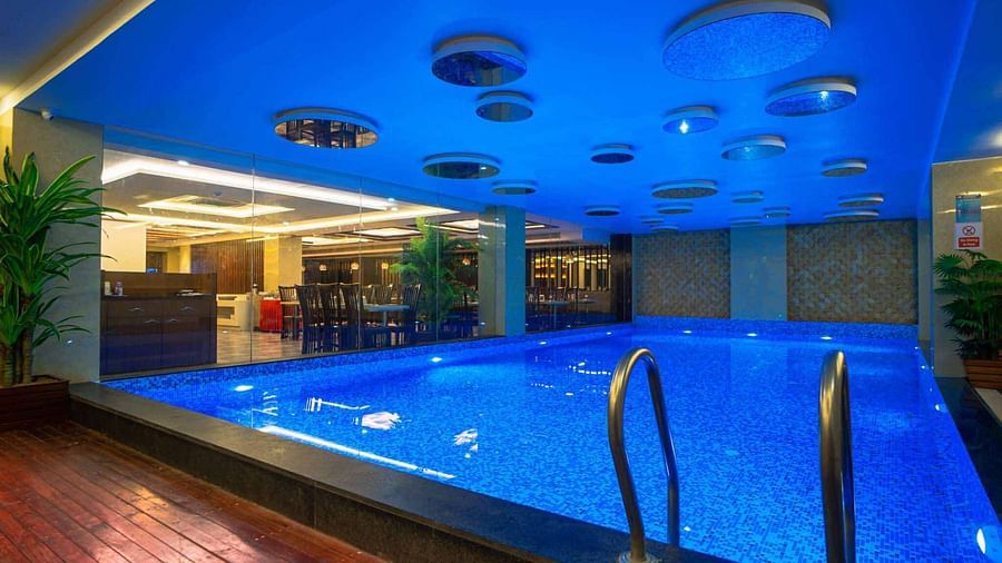 An indoor swimming pool with blue water and a blue ceiling, illuminated by warm lighting at Mansha Hotel Regency.