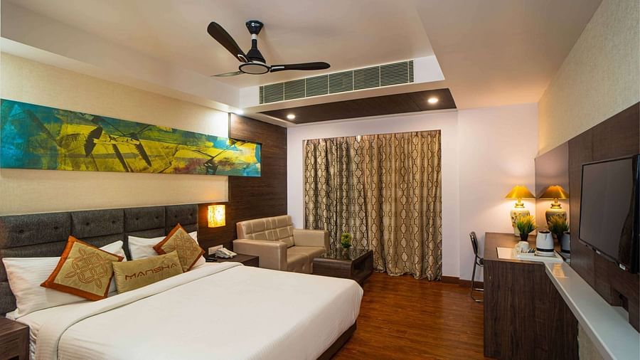 A room with a bed, a sofa, a wall-mounted television, and a ceiling fan at Mansha Hotel Regency.