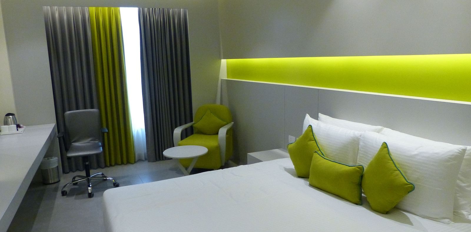  Spacious twin beds with headboards line the wall, large windows with curtains cover them, and a sofa is placed near the window