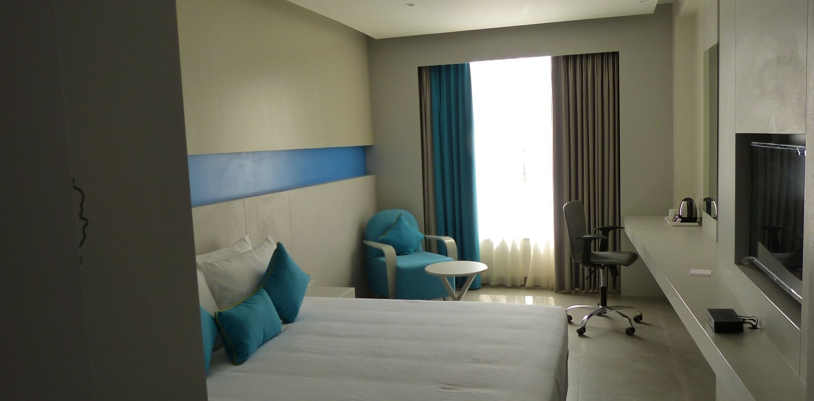  Spacious twin beds with headboards line the wall, large windows with curtains cover them, and a sofa is placed near the window