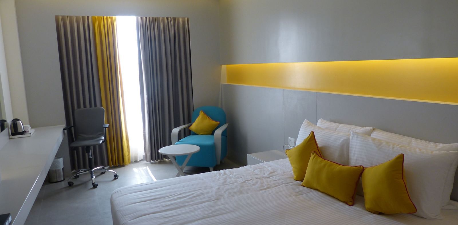  Spacious twin beds with headboards line the wall, large windows with curtains cover them, and a sofa is placed near the window