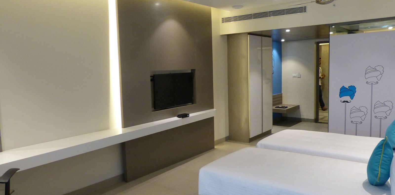 A twin bed faces a wall-mounted television directly opposite
