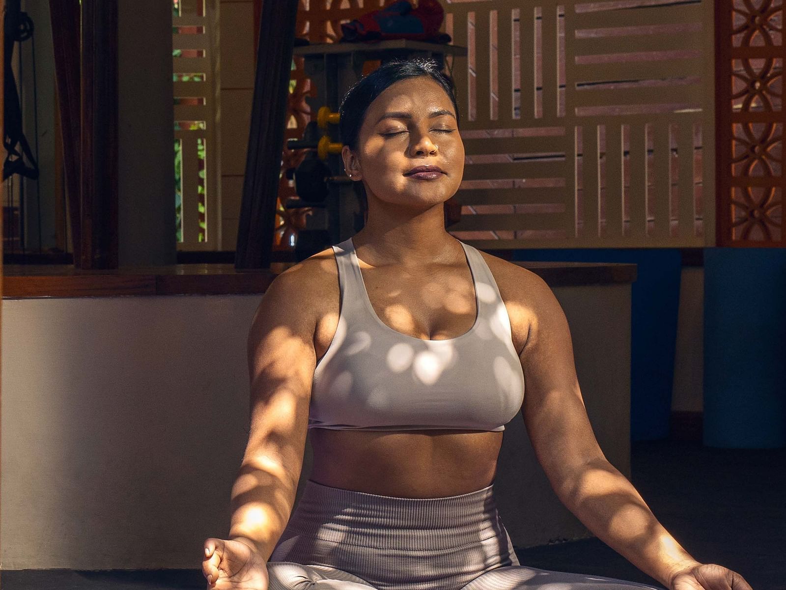 A portrait shot of a  woman meditating in a peaceful shady room, on a yoga mat.