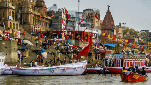 A colorful and bustling riverside view of Varanasi with boats and temples.