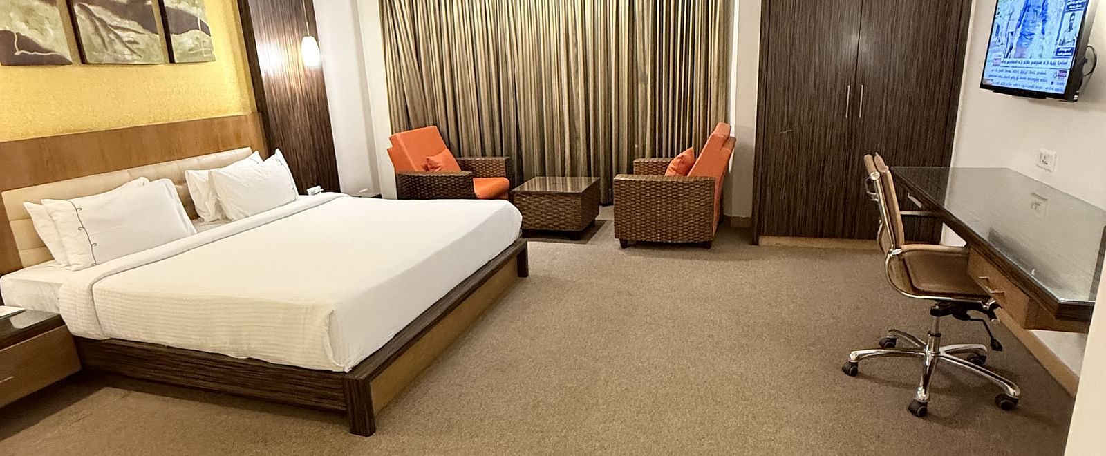 A spacious room with a large bed, cushioned seating beside the window with curtains, and a TV with a writing desk to the side | Cenneys Gateway