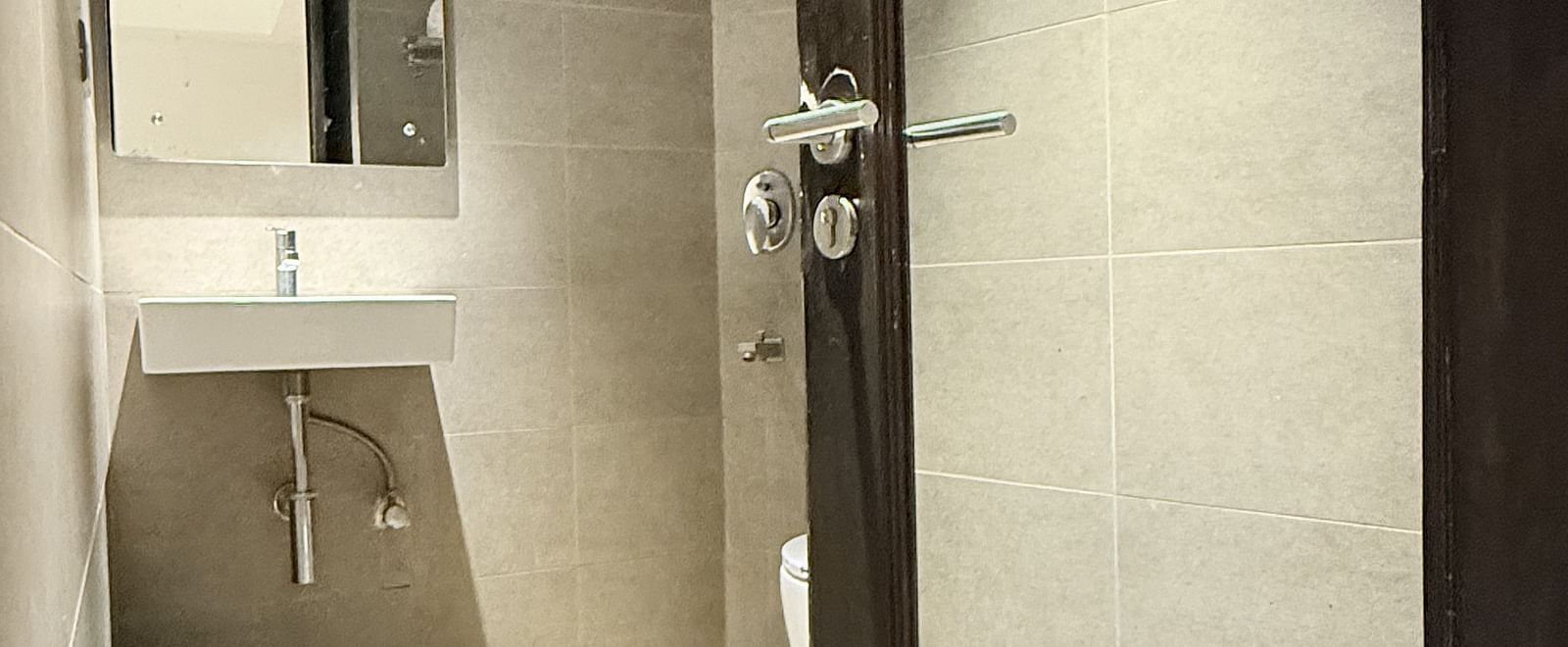 A spacious washroom with a wall-mounted mirror above the washbasin and an open door for entry | Cenneys Gateway