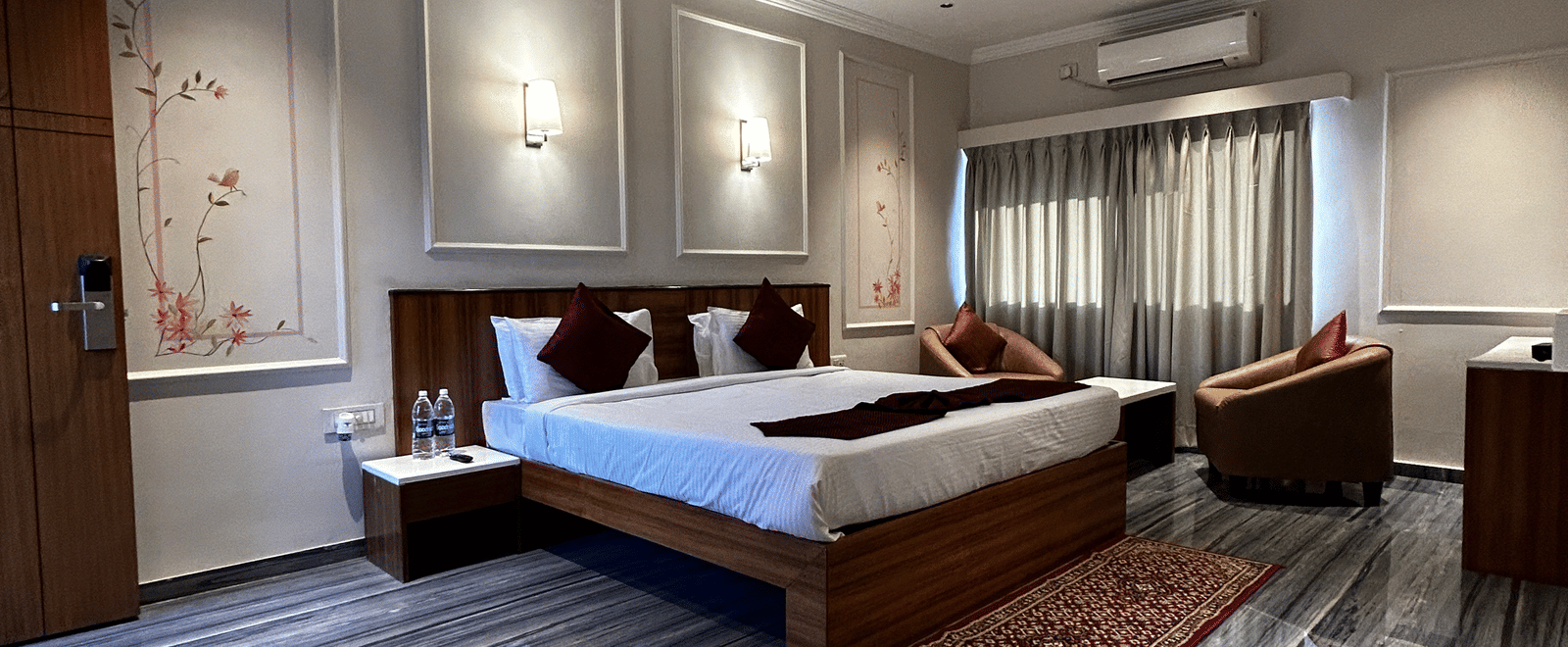 A spacious hotel suite with polished grey marbled flooring, a wooden bed, and a separate seating area at Pravasa Hotel, Kolhapur. 