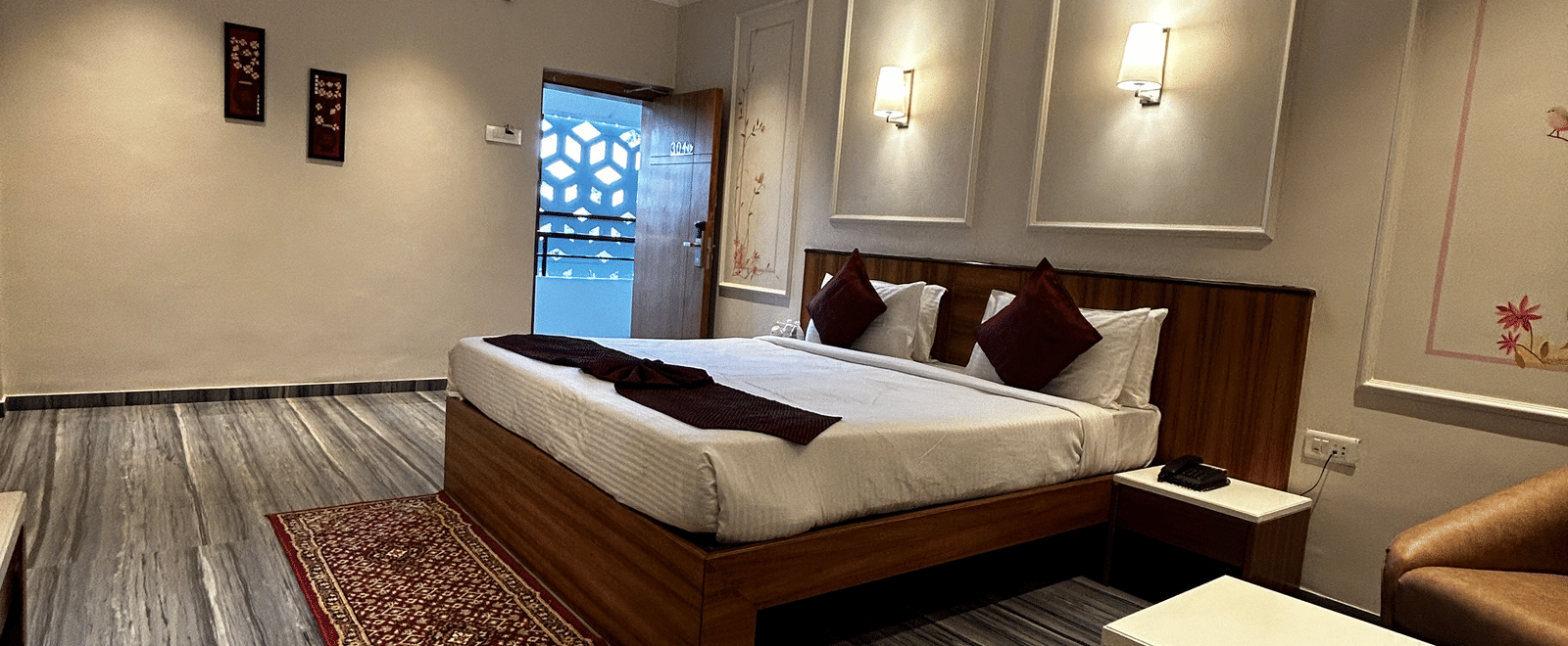 A comfortable hotel room featuring a double bed, tan armchair seating, and grey marble-effect flooring at Pravasa Hotel, Kolhapur.
