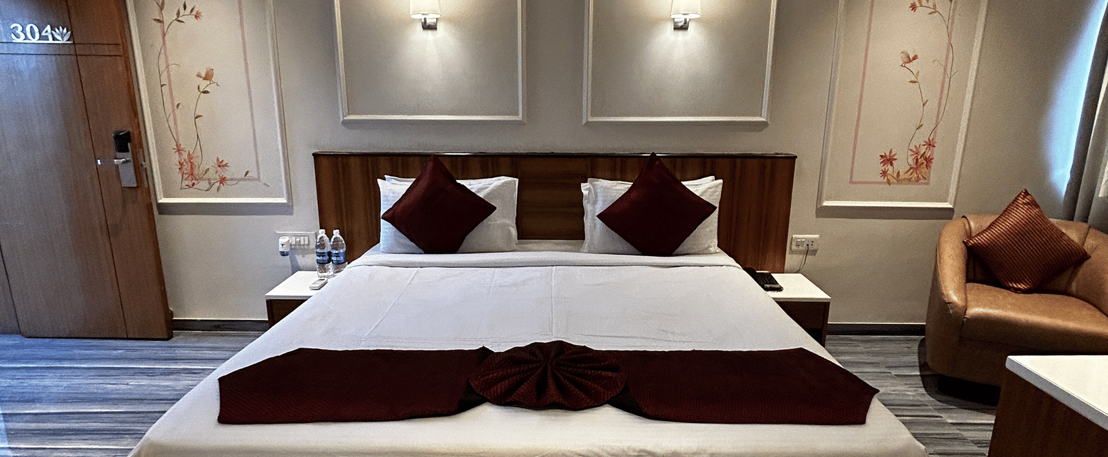A modern hotel room featuring a double bed, red and white bedding, and two recessed panel lights at Pravasa Hotel, Kolhapur.