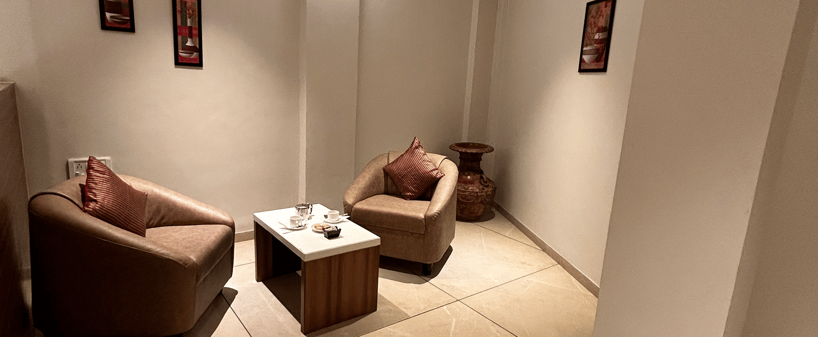 A simple and private meeting or waiting area with two curved chairs and a small dark wood table at Pravasa Hotel, Kolhapur.