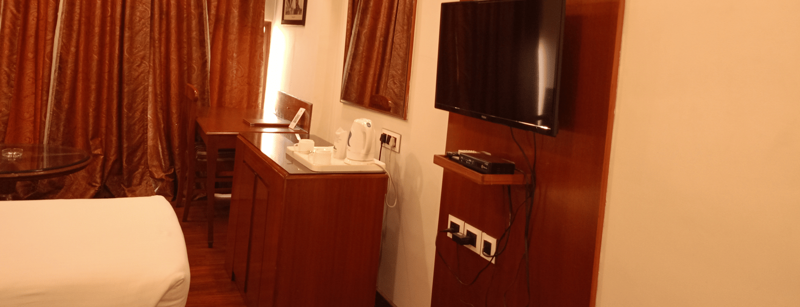 Room at Hotel Gold, Panipat with a bed, TV, desk, and curtains along the window.