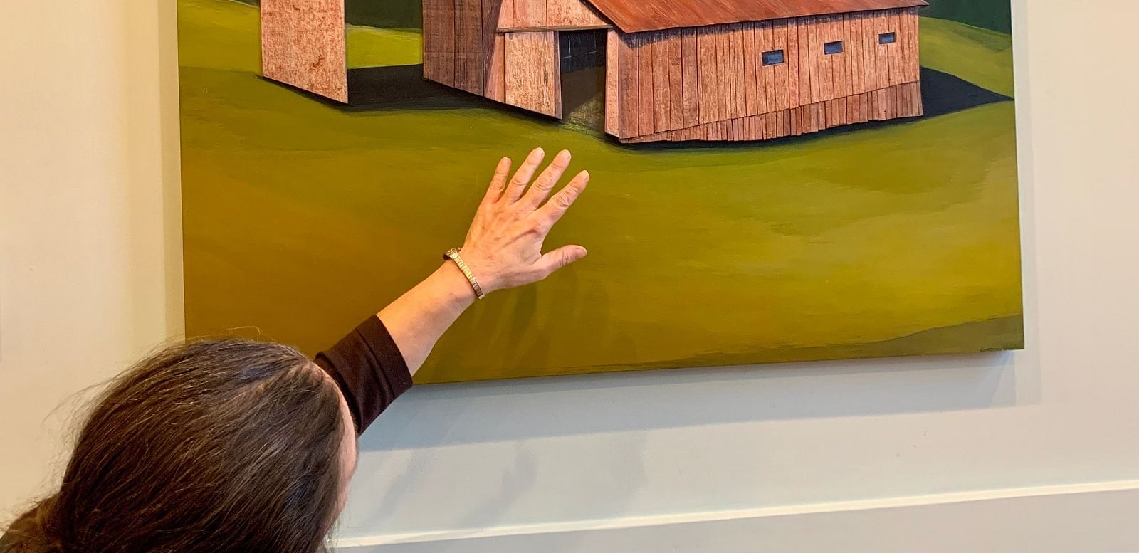 A person pointing at a painting of a rustic barn displayed in an art gallery.