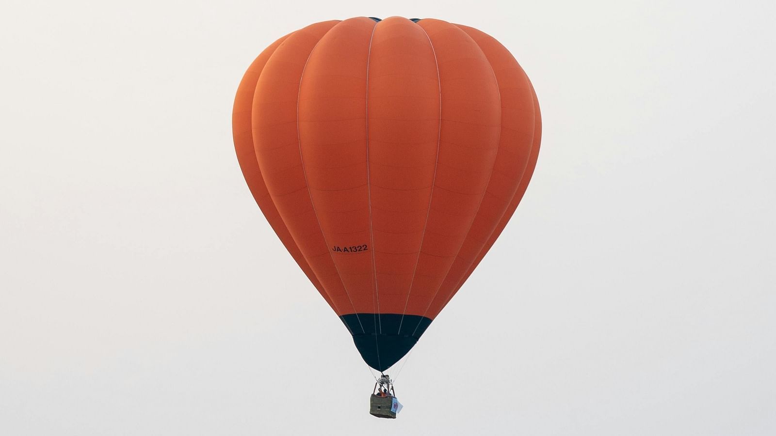A single orange hot air balloon floats in the sky above a misty landscape.