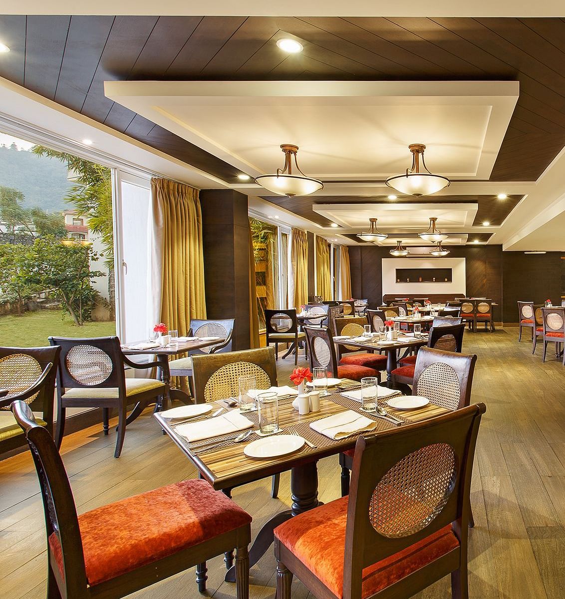 A spacious restaurant with a wooden floor and exposed wooden beams on the ceiling. Large windows offer views of the outdoors.