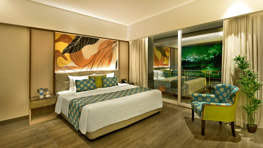 Bright guest room with king bed, green accents and large window at The Sonnet, Jamshedpur.
