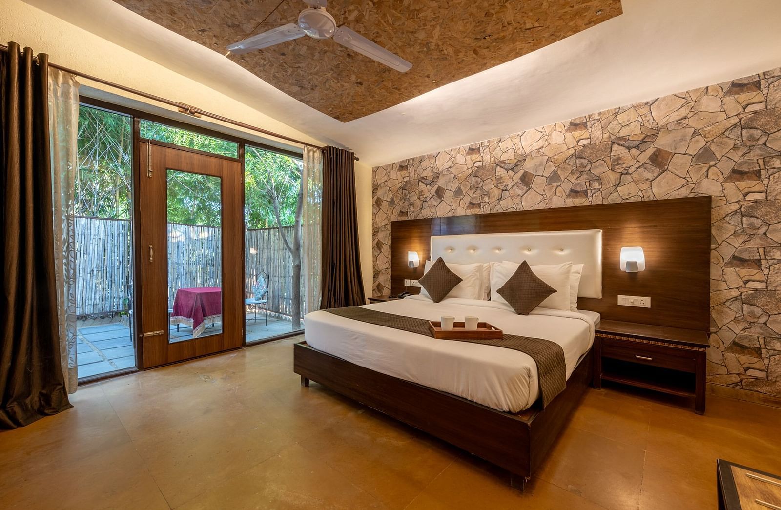 A room with a bed, lamps on the headboard, a ceiling fan, large glass doors with curtains at Valley by Grassfield 