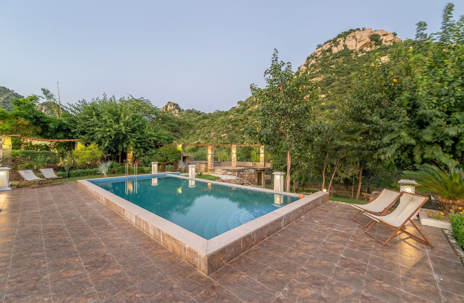 An outdoor pool at Valley by Grassfield, surrounded by plants and trees, with two lounge chairs on the side.