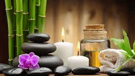 Spa products featuring massage stones, a candle burning, massage oil, towel, and other things.