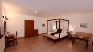 The room features a spacious layout with a four-poster bed, a cosy sofa, and a wooden desk with a chair. - Abad Brookside Lakkidi, Wayanad