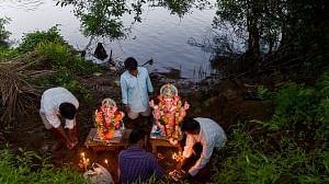 Several people are gathered near a body of water, preparing to immerse idols.