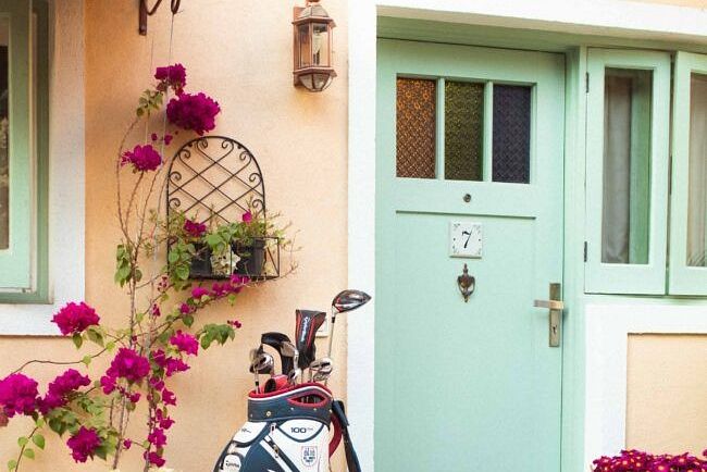 Entrance to a pastel coloured villa with a mint green door, potted flowers, and golf bags near the wall at Karma Chalets.