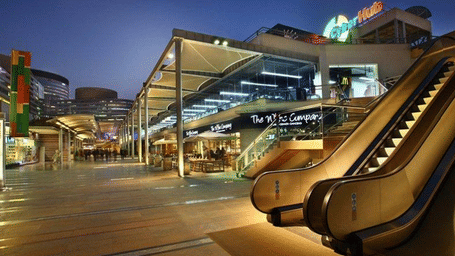 Evening view of CyberHub Gurgaon featuring illuminated restaurants, open-air walkways, and an escalator with people enjoying dining and leisure spaces.