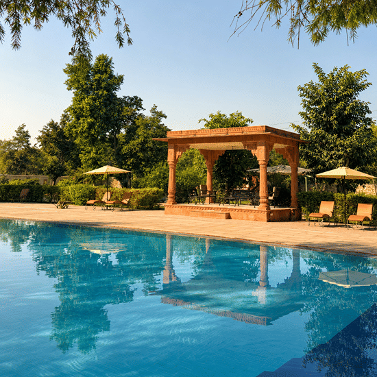 The blue swimming pool at Umaid Palace, bordered by terracotta paving, leafy trees and a sandstone pavilion.