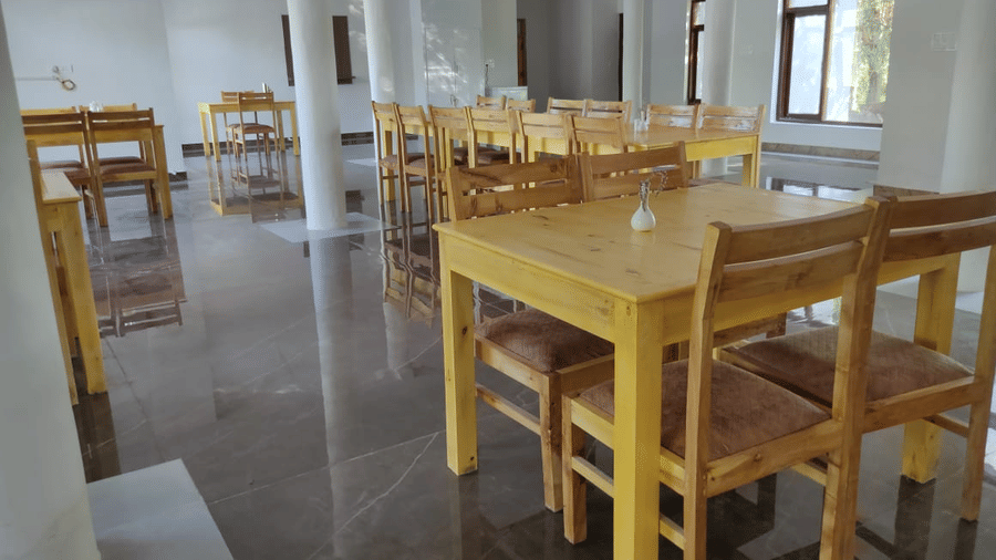 A view of the spacious dining hall featuring light-coloured wooden tables and structural white pillars at Indus Serenity Retreat.