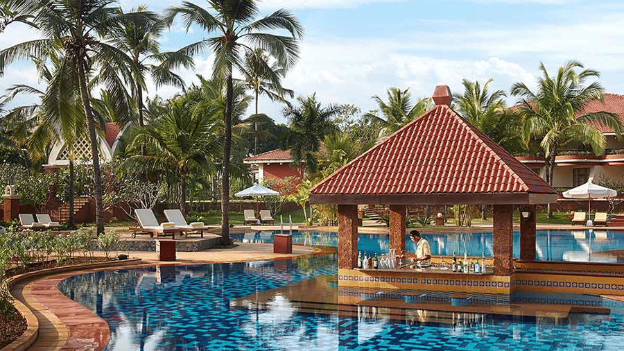 A view of the Island Bar at Caravela Beach Resort, Goa, with a canopy int he centre and coconut trees in the background, on a sunny day.