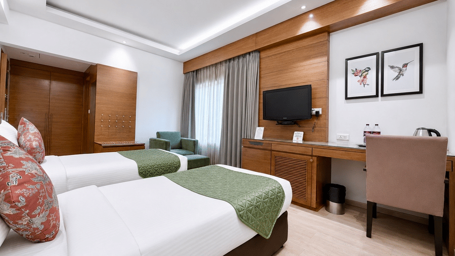 Deluxe Room with twin beds, green accents, and a functional work desk at Hotel Saket 27, offering a comfortable and modern stay.