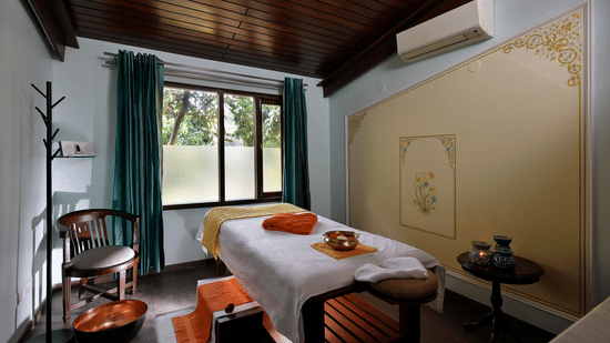 A wide-angle shot of the spa room featuring a spa bed in the centre with ample of natural light coming inside from the window at Neemrana's Glasshouse on The Ganges, Rishikesh.