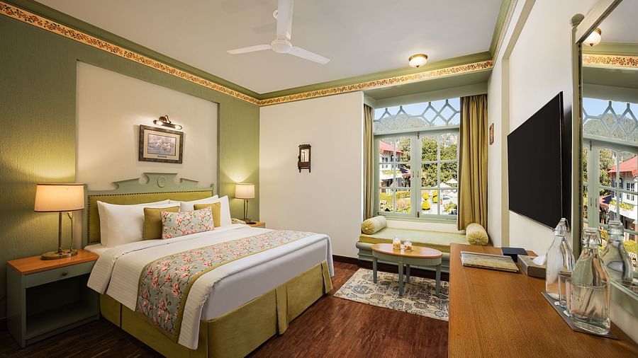 An image of a  cozy room in the naini retreat, nainital, with a king-size bed, wooden furniture, and a window. The room also features a ceiling fan, a TV and wooden flooring.