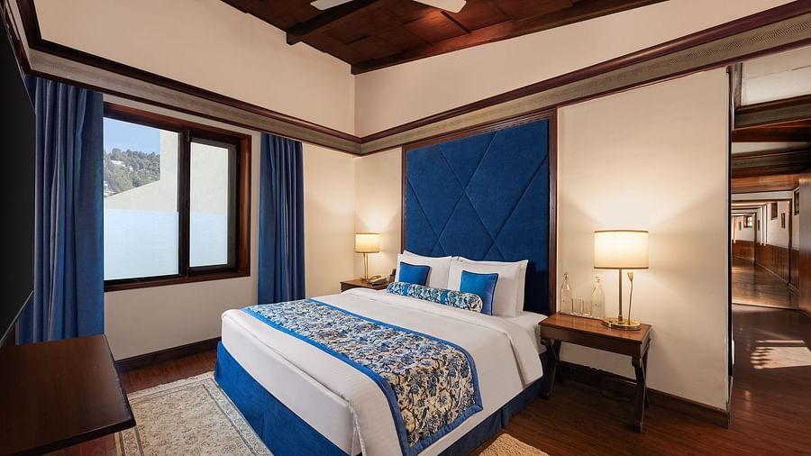 An image of a  cozy room in the naini retreat, nainital, with a king-size bed, wooden furniture, and a window. The room also features a ceiling fan.